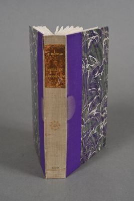 an old book with a purple cover sitting on top of a table