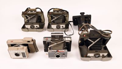 several old cameras are lined up in a row on a white surface