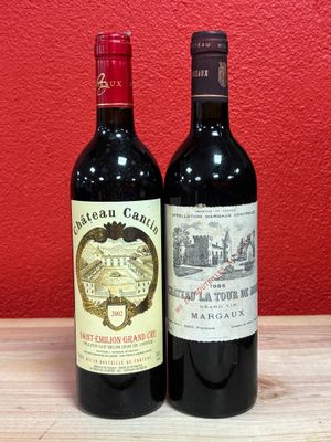 two bottles of wine sitting on top of a wooden table next to a red wall