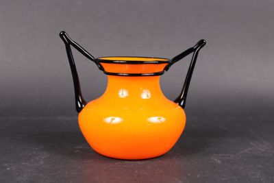an orange vase with a black handle on a table