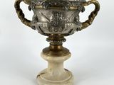 un vase ancien en argent et marbre posé sur un socle, sur fond blanc