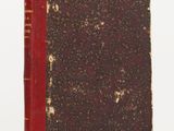 an old book sitting on top of a white table next to a red book