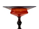 an orange and black glass bowl on a black pedestal