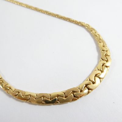 le collier en or est posé sur une surface blanche, devant un fond blanc