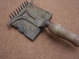 une petite brosse métallique avec un manche en bois posée sur une surface marron