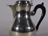 une cafetière ancienne en argent avec une poignée noire, posée sur une table