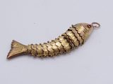 a close up of a gold fish pendant on a white surface