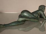 a bronze statue of a woman laying on a glass table