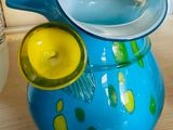 a blue glass pitcher with a yellow lid on a table next to a glass jar