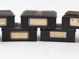 six petites boîtes noires ornées d'étiquettes dorées sont empilées les unes sur les autres