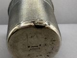 un récipient argenté posé sur une surface blanche