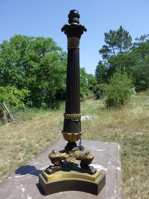 une horloge noire et dorée posée sur un socle au milieu d'un champ