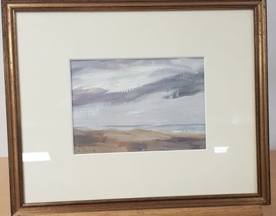tableau représentant une scène de plage, dans un cadre doré, posé sur une table en bois