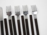 six forks and a knife are lined up on a white surface