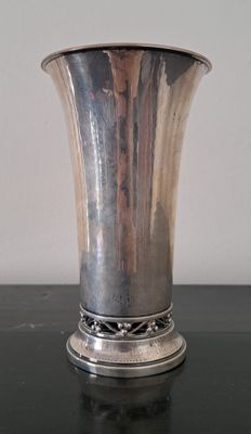 un vase en argent posé sur une table noire, avec un mur blanc en arrière-plan