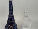 un flacon de parfum en forme de Tour Eiffel bleu et or à côté d'un flacon en verre transparent