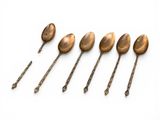 six antique spoons are lined up in a row on a white surface