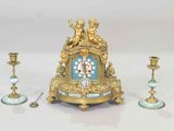 a gold clock sitting on top of a table next to two candles