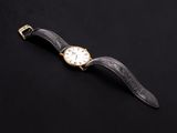 a gold watch with a black leather strap on a black background