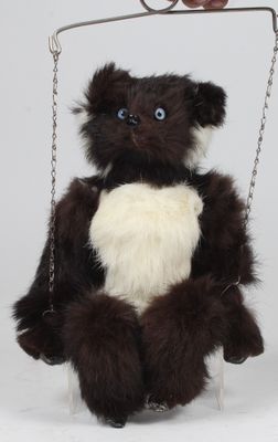 un ours en peluche assis sur une balançoire, avec un cœur sur la poitrine