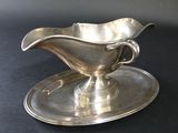 a silver gravy on a silver plate on a black table
