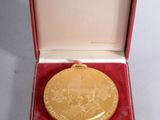 l'image d'une médaille d'or dans un coffret rouge posé sur un fond blanc