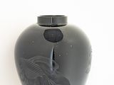 a black vase with a bird on it on a white surface