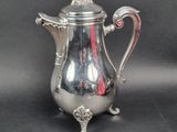 an antique silver coffee pot with a red handle on a black background