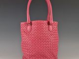 a pink handbag with a woven handle on a grey background