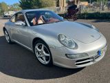 une Porsche argentée garée sur un parking, avec une calèche en arrière-plan