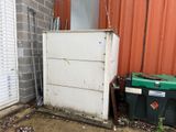 a white refrigerator sitting outside of a building next to a green trash can