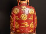 statue of a man in a red and gold outfit sitting on a wooden stand
