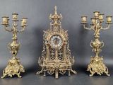 three gold colored candlesticks and a clock on a table