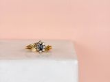 un gros plan d'une bague en or sertie d'un diamant bleu, posée sur un bloc blanc