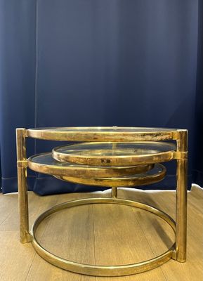 une table basse ronde en laiton avec un plateau en verre, posée sur un parquet