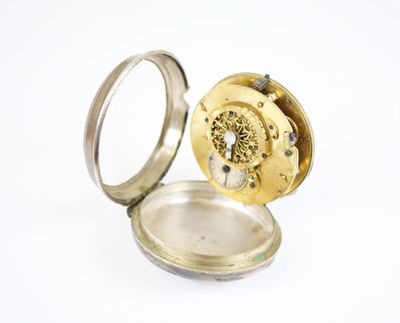 une petite montre de poche en argent posée à l'intérieur, sur une surface blanche