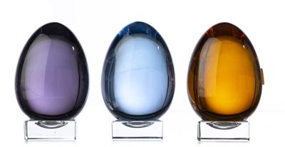 trois vases en verre en forme d'œuf posés sur un socle transparent