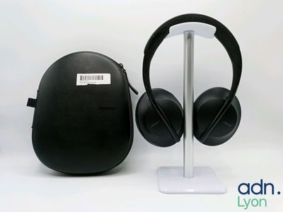 deux casques audio noirs posés sur un support blanc à côté d'un étui noir