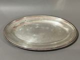 an oval silver plate with a beaded edge on a gray surface