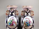 two vases with a painting of people on them sitting on a table