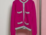 pink cardigan sweater hanging on a hanger in front of a pink wall