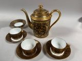 une théière en or et quatre tasses posées sur une table blanche