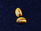 two yellow tiger eye beads on a black surface