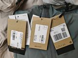 three tags hang on a jacket on a bed next to a pair of pants