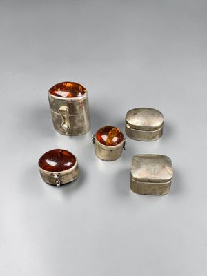 quatre bagues en argent et ambre et deux boîtes en argent posées sur un fond blanc