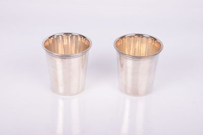 une paire de verres à shot en métal argenté posés sur un support blanc