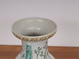 a white vase with a green bird on it sitting on a table