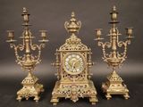 trois bougeoirs dorés et une horloge posés sur une table