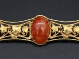 a close up of a gold and red stone broochle