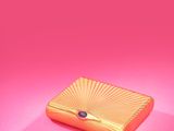 a gold clutch bag with a blue eye on a pink background